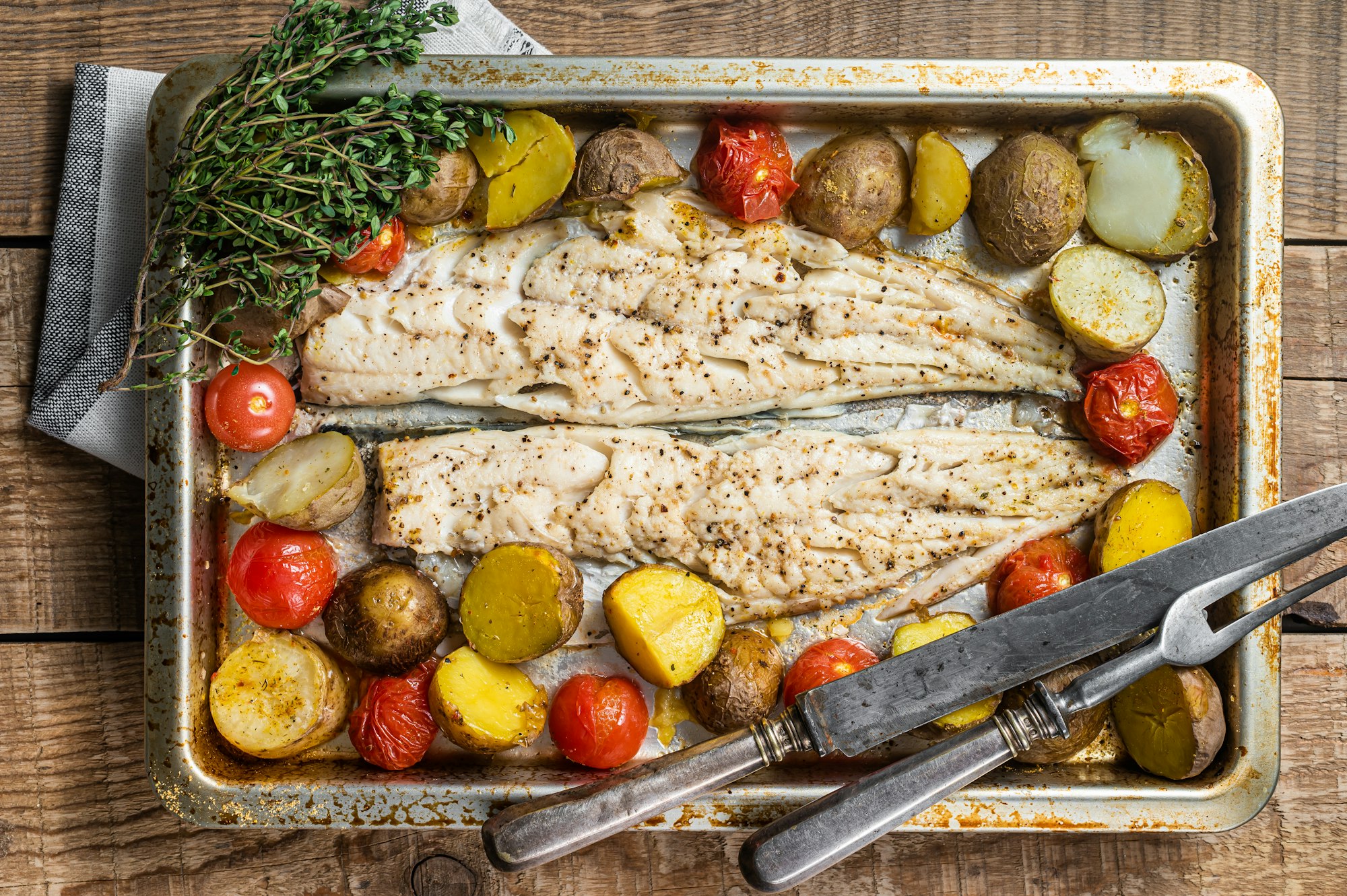 Hake fish fillet, roasted fish meat with tomato and potato. Wooden background. Top view